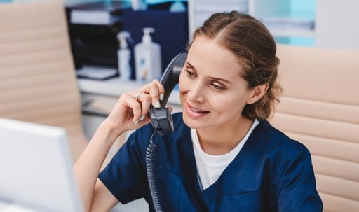Young-female-receptionist-talking-on-phone-in-clinic-while-sitting-and-looking-on-pc-monitor-1275072681_2123x1416-1-1